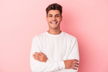 Pembe arka planda izole edilmiş genç beyaz adam kendini güvende hissediyor, kararlılıkla kollarını kavuşturuyor..