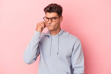 Pembe arka planda izole edilmiş genç beyaz bir adam parmakları dudaklarında bir sır saklıyor..