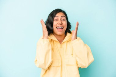 Mavi arka planda izole edilmiş genç Latin kadın yüksek sesle gülüyor elini göğsüne koyuyor..