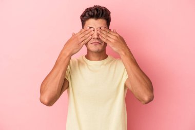 Pembe arka planda izole edilmiş genç beyaz adam elleriyle gözlerini kapatmaktan korkuyor..
