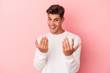Pembe arka planda izole edilmiş genç beyaz adam sanki seni davet ediyormuş gibi seni işaret ediyor..