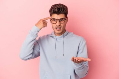 Pembe arka planda izole edilmiş genç beyaz adam elinde bir ürün tutuyor..