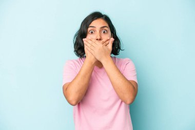 Mavi arka planda izole edilmiş genç Latin kadın elleriyle ağzını kapatırken şok oldu..