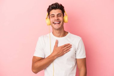 Pembe arka planda izole edilmiş müzik dinleyen beyaz bir adam yüksek sesle gülüyor ve elini göğsüne koyuyor..