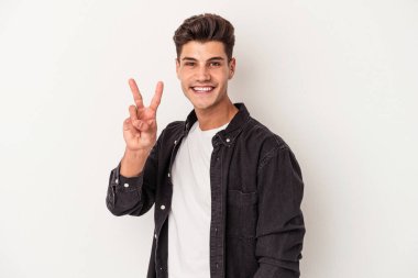 Beyaz arka planda izole edilmiş genç beyaz bir adam zafer işareti gösteriyor ve gülümsüyor..