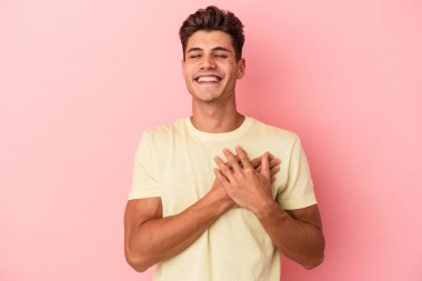 Pembe arka planda izole olmuş genç beyaz adam gülüyor, elini yüreğine koyuyor, mutluluk kavramını koruyor..