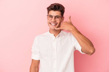 Pembe arka planda izole edilmiş genç beyaz adam parmaklarıyla bir cep telefonu hareketi gösteriyor..