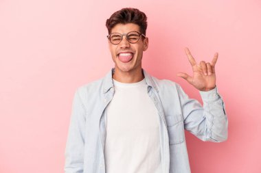 Pembe arka planda izole edilmiş genç beyaz adam parmaklarıyla taş hareketi gösteriyor.