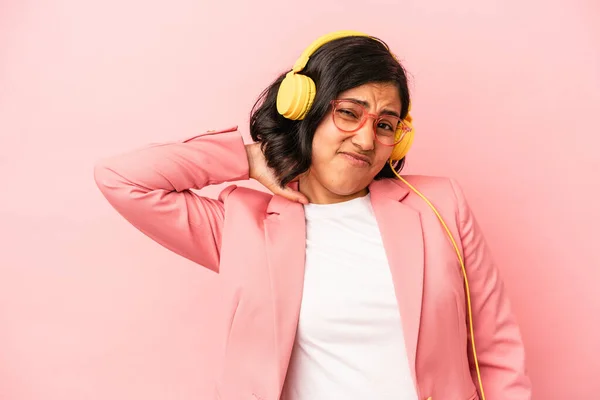 Young latin woman listening to music isolated on pink background touching back of head, thinking and making a choice.