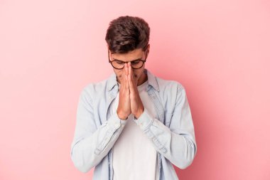 Genç beyaz adam pembe arka planda izole edilmiş dua ediyor, bağlılık gösteriyor, dindar biri ilahi ilham arıyor..