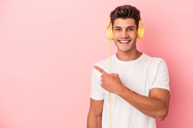 Pembe arka planda izole edilmiş müzik dinleyen beyaz bir adam gülümsüyor ve boş alanda bir şeyler gösteriyor..
