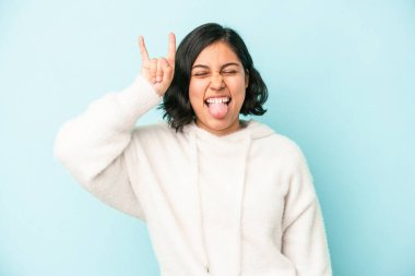 Mavi arka planda izole edilmiş genç Latin kadın parmaklarıyla taş hareketi gösteriyor.