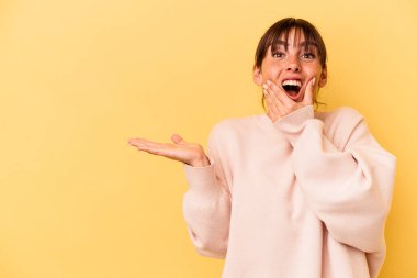 Sarı arka planda izole edilmiş genç Arjantinli kadın avuç içinde fotokopi alanı tutuyor, el üstünde tutuyor. Şaşırmış ve mutlu..