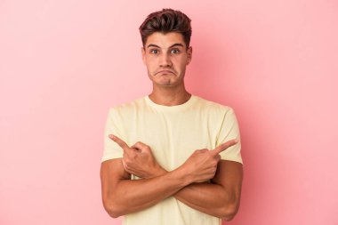 Pembe arka plan noktalarında izole edilmiş genç beyaz adam iki seçenek arasında seçim yapmaya çalışıyor..