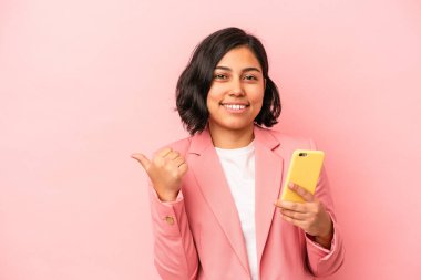 Elinde cep telefonu tutan genç Latin kadın pembe arka planda izole edilmiş gülümsüyor ve başparmağını kaldırıyor.