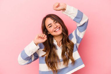 Pembe arka planda soyutlanmış genç beyaz bir kadın özel bir günü kutluyor, atlıyor ve enerjiyle kollarını kaldırıyor..