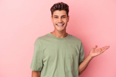 Pembe arka planda izole edilmiş genç beyaz bir adam bir palmiye üzerinde fotokopi alanı ve belinde başka bir el tutuyor..