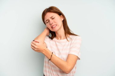 Genç İngiliz kadın, mavi arka planda izole edilmiş, dirsek masajı yapıyor, kötü bir hareketin ardından acı çekiyor..