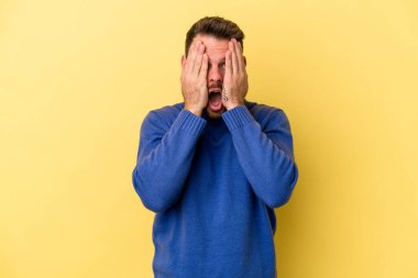 Sarı arka planda izole edilmiş genç beyaz adam yüzünün yarısını palmiye ile örterek eğleniyor..