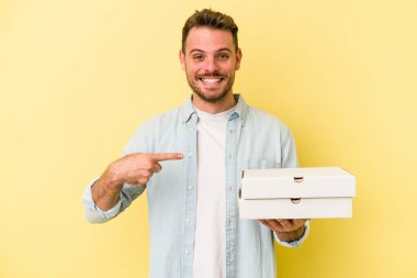 Sarı arka planda izole edilmiş pizzalar tutan beyaz bir adam gömlek fotokopi odasını işaret ediyor, gururlu ve kendinden emin