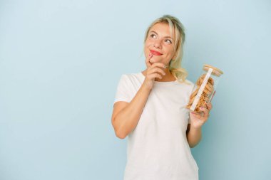 Elinde mavi arka planda izole edilmiş kurabiyeler tutan genç Rus kadın şüpheli ve kuşkulu bir ifadeyle yana bakıyor..