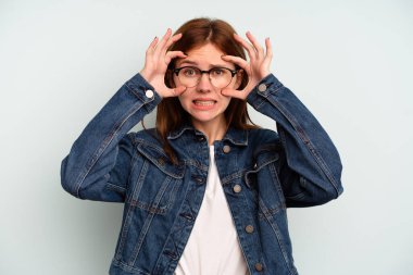 Mavi arka planda izole edilmiş genç bir İngiliz kadın bir başarı fırsatı bulmak için gözlerini açık tutuyor..