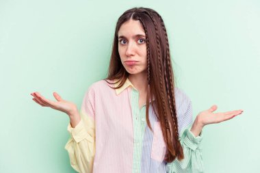 Kafkasyalı genç bir kadın yeşil arka planda izole edilmiş sorgulama sırasında omuz silkiyor ve kuşkulanıyor..