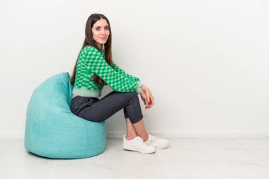 Beyaz arka planda izole edilmiş beyaz bir puf üzerinde oturan beyaz bir kadın.