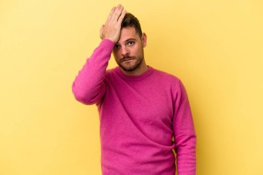 Sarı arka planda izole edilmiş genç beyaz bir adam bir şeyi unutuyor. Alnına avuç içi ve gözlerini kapayarak vuruyor..