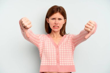 Mavi arka planda izole edilmiş genç bir İngiliz kadın baş parmağını aşağı gösteriyor ve hoşlanmadığını ifade ediyor..