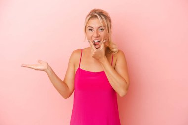 Pembe arka planda izole edilmiş genç Rus kadın avuç içinde fotokopi alanı tutuyor, el üstünde tutuyor. Şaşırmış ve mutlu..
