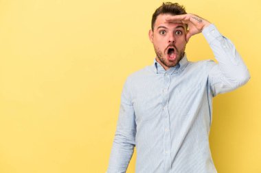 Kafkasyalı genç adam sarı arka planda izole edilmiş, uzaklara bakıyor ve elini alnına koyuyor..