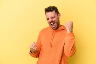 Sarı arka planda izole edilmiş genç beyaz adam tasasız ve heyecanlı bir şekilde tezahürat yapıyor. Zafer konsepti.
