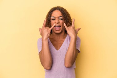 Sarı arka planda izole edilmiş genç Latin transseksüel kadın bir devrim konsepti olarak boynuz hareketi gösteriyor..