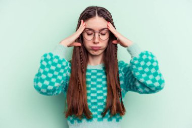 Genç beyaz kadın yeşil arka planda izole edilmiş tapınaklara dokunuyor ve baş ağrısı çekiyor..