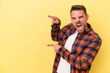 Sarı arka planda izole edilmiş genç beyaz adam işaret fişekleriyle işaret ederek heyecanlanıyor..