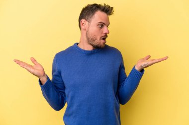 Kafkasyalı genç adam sarı arka planda izole edilmiş. Kafası karışmış ve omuz silkiyor. Kopya alanını tutmak için..