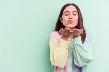 Genç beyaz kadın yeşil arka planda izole edilmiş dudaklar kıvrılmış ve hava öpücüğü vermek için avuç içleri tutulmuş..