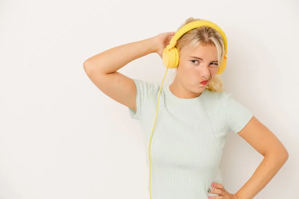 Young Russian woman listening to music isolated on white background touching back of head, thinking and making a choice.
