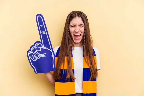 Young sports fan woman isolated on yellow background screaming very angry and aggressive.