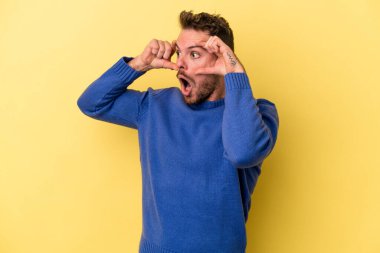 Sarı arka planda izole edilmiş genç beyaz adam bir başarı fırsatı bulmak için gözlerini açık tutuyor..