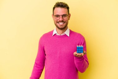 Rubiks küpünü tutan genç beyaz adam arka planda izole edilmiş mutlu, güler yüzlü ve neşeli..