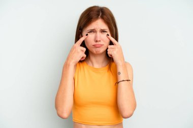 Genç İngiliz kadın mavi arka planda izole edilmiş ağlıyor, bir şeyden memnun değil, acı ve kafa karışıklığı konsepti..