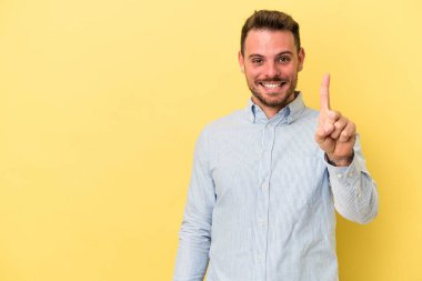Sarı arka planda izole genç beyaz adam parmak ile bir numara gösteriyor.