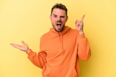 Genç beyaz adam sarı arka planda izole edilmiş ve elinde bir ürün var..