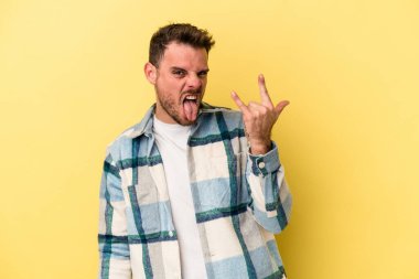 Sarı arka planda izole edilmiş genç beyaz adam parmaklarıyla kaya hareketi gösteriyor.