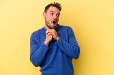 Sarı arka planda izole edilmiş genç beyaz adam ellerini çenesinin altında tutuyor ve mutlu bir şekilde yan tarafa bakıyor..