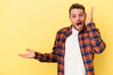 Sarı arka planda izole edilmiş genç beyaz bir adam bir avuç içinde fotokopi alanı tutuyor, el üstünde tutuyor. Şaşırmış ve mutlu..