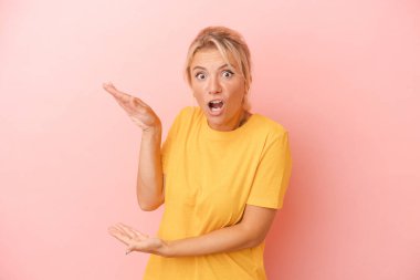 Pembe arka planda izole edilmiş genç bir Rus kadın elleri arasında bir kopya alanı tutarken şok olmuş ve hayrete düşmüş..