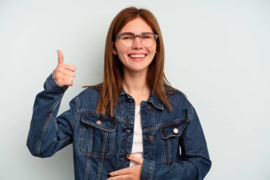 Mavi arka planda izole edilmiş genç İngiliz kadın karnına dokunuyor, nazikçe gülümsüyor, yemek yiyor ve tatmin oluyor..